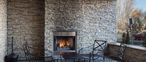 An outdoor seating area with stone walls, a fireplace, and metal chairs.