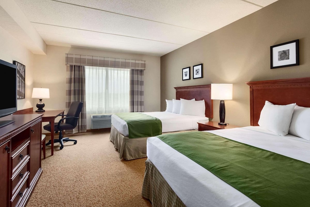 A hotel room with two beds, a desk, a chair, and a television.