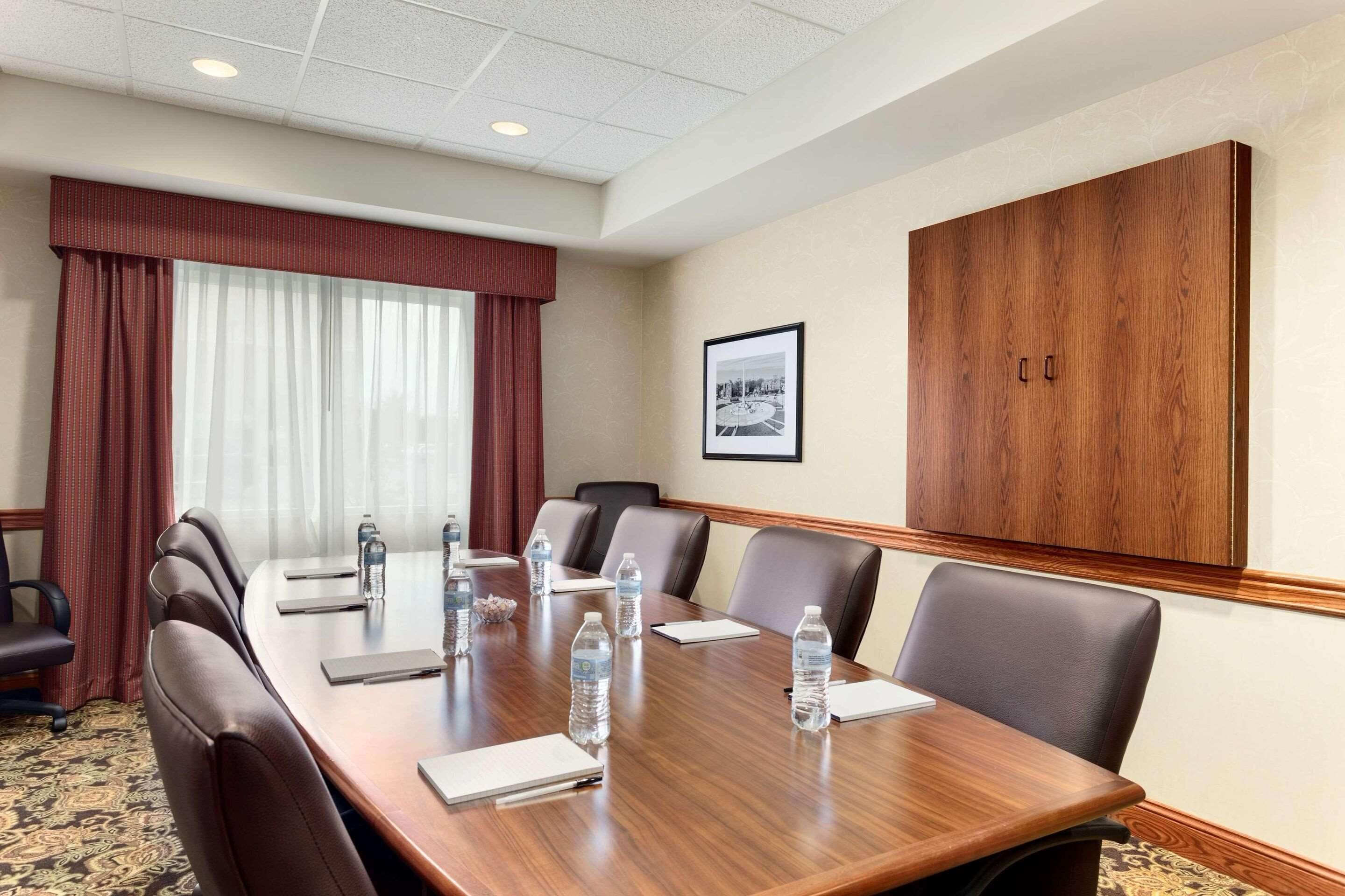 A conference room with a long table, leather chairs, water bottles, and a large wooden cabinet.