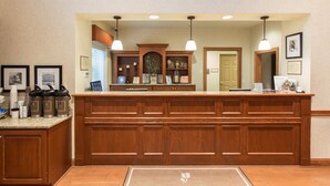 A reception area with a wooden reception desk, framed pictures on the wall, and a welcome mat on the floor. - Country Inn & Suites by Radisson, Buffalo South I-90, NY (Buffalo)