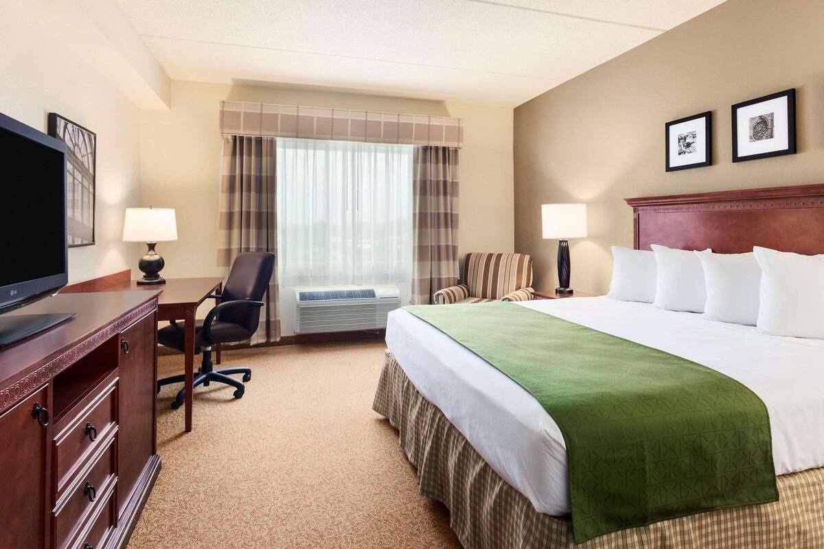A hotel room with a bed, a desk, a chair, a television, and a window with curtains.