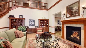 A spacious living room with a fireplace, a wooden staircase, and a large mirror. - Country Inn & Suites by Radisson, Buffalo South I-90, NY (Buffalo)