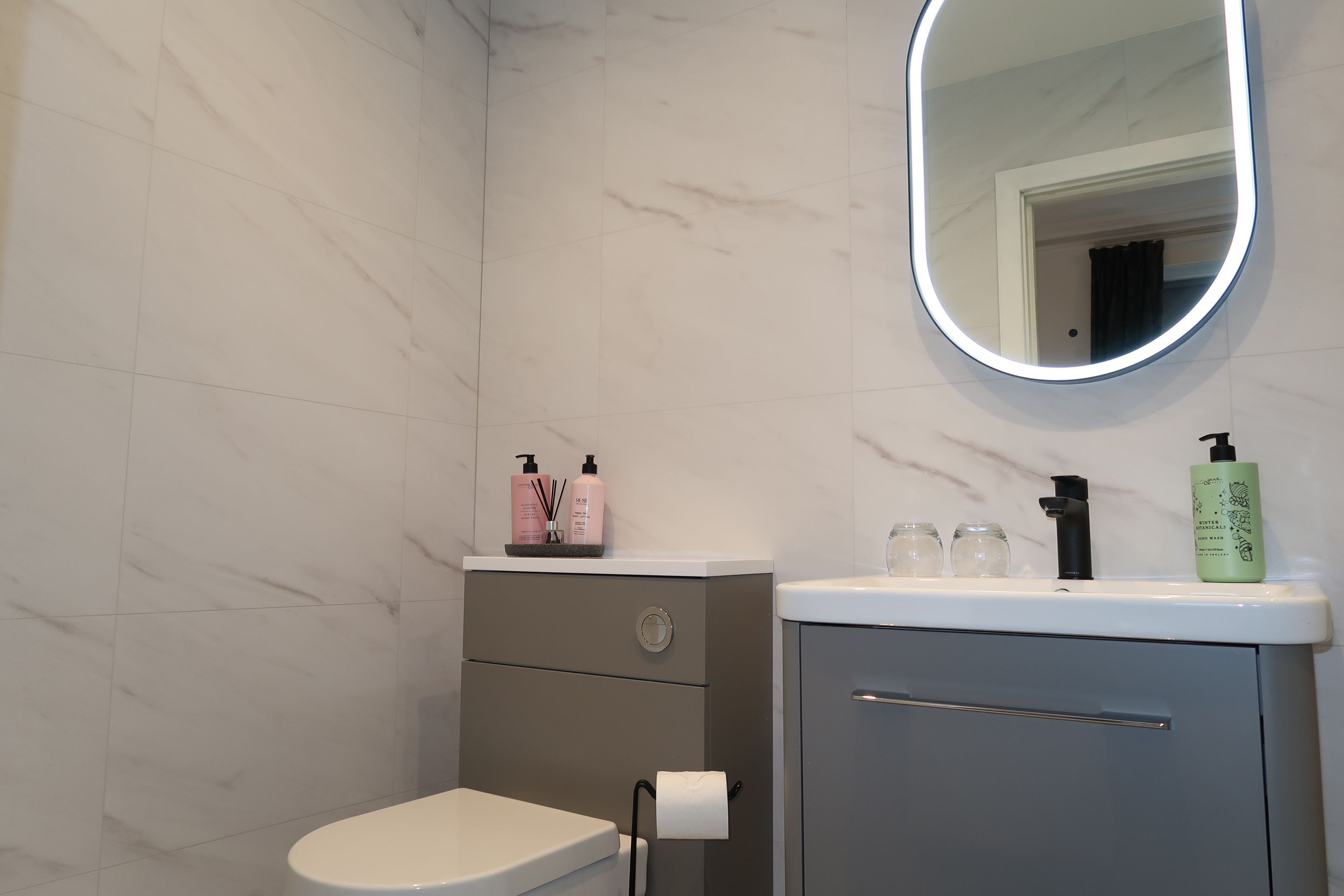 A bathroom with a toilet, a sink, a mirror, and toiletries on the counter.
