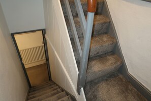 A carpeted staircase with a handrail and a door leading to a room with a radiator. - Abbey House Bed and Breakfast (Penrith)
