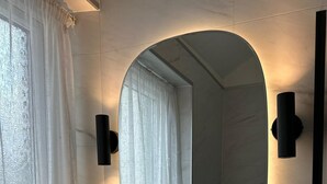 A bathroom with a white sink, a round mirror, and a window with white curtains. - Abbey House Bed and Breakfast (Penrith)