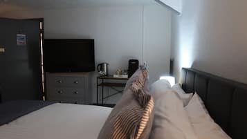 Quarto de hotel com cama, escrivaninha com chaleira, televisão e placa de sinalização de combate a incêndio na porta.