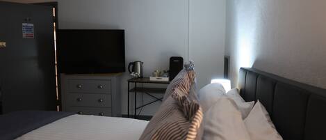 Habitación de hotel con cama, escritorio con hervidor, televisión y señal de procedimientos de emergencia contra incendios en la puerta.