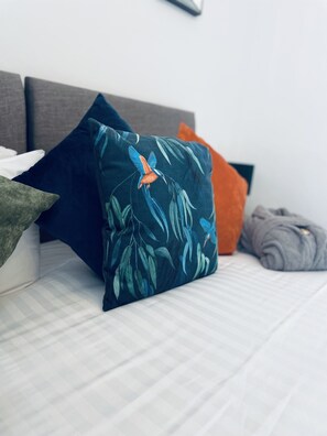 A bed with a striped mattress, a grey headboard, and multiple pillows including one with a bird design. - Abbey House Bed and Breakfast (Penrith)