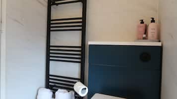 Casa de banho com porta-toalhas, sanita e produtos de higiene numa estante.