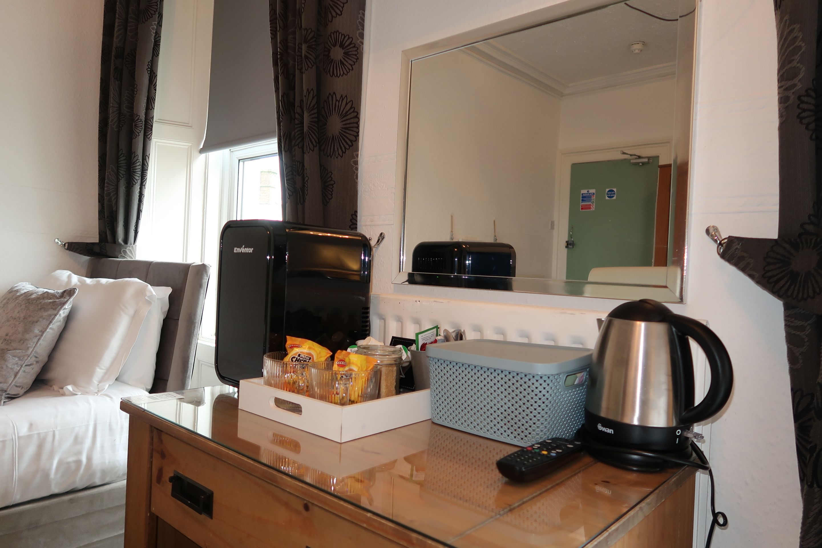 Quarto de hotel com cama, escrivaninha, cafeteira, torradeira e espelho.