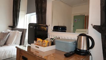 Quarto de hotel com cama, escrivaninha, cafeteira, torradeira e espelho.