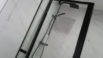 A glass-enclosed shower with a handheld showerhead and a fixed overhead rainhead.