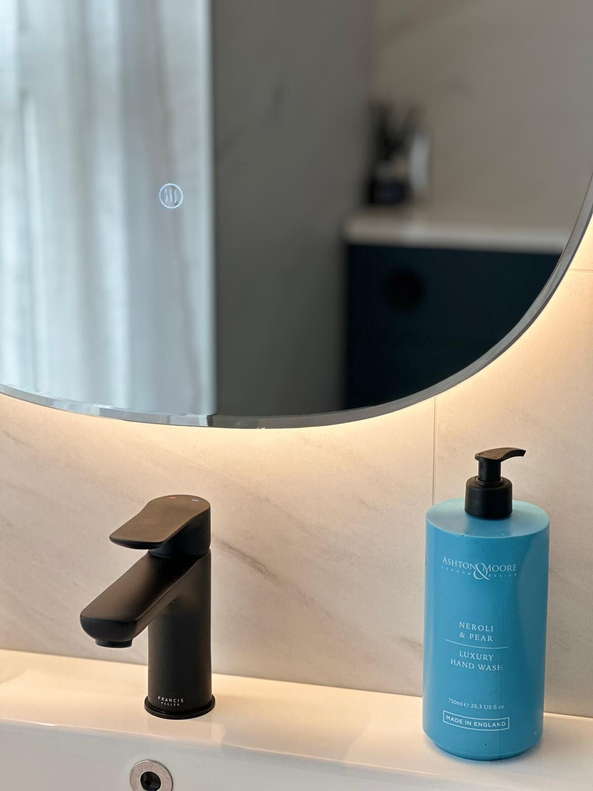 Casa de banho moderna com uma torneira preta, um frasco azul de lavagem para as mãos e um espelho a refletir um armário de casa de banho.