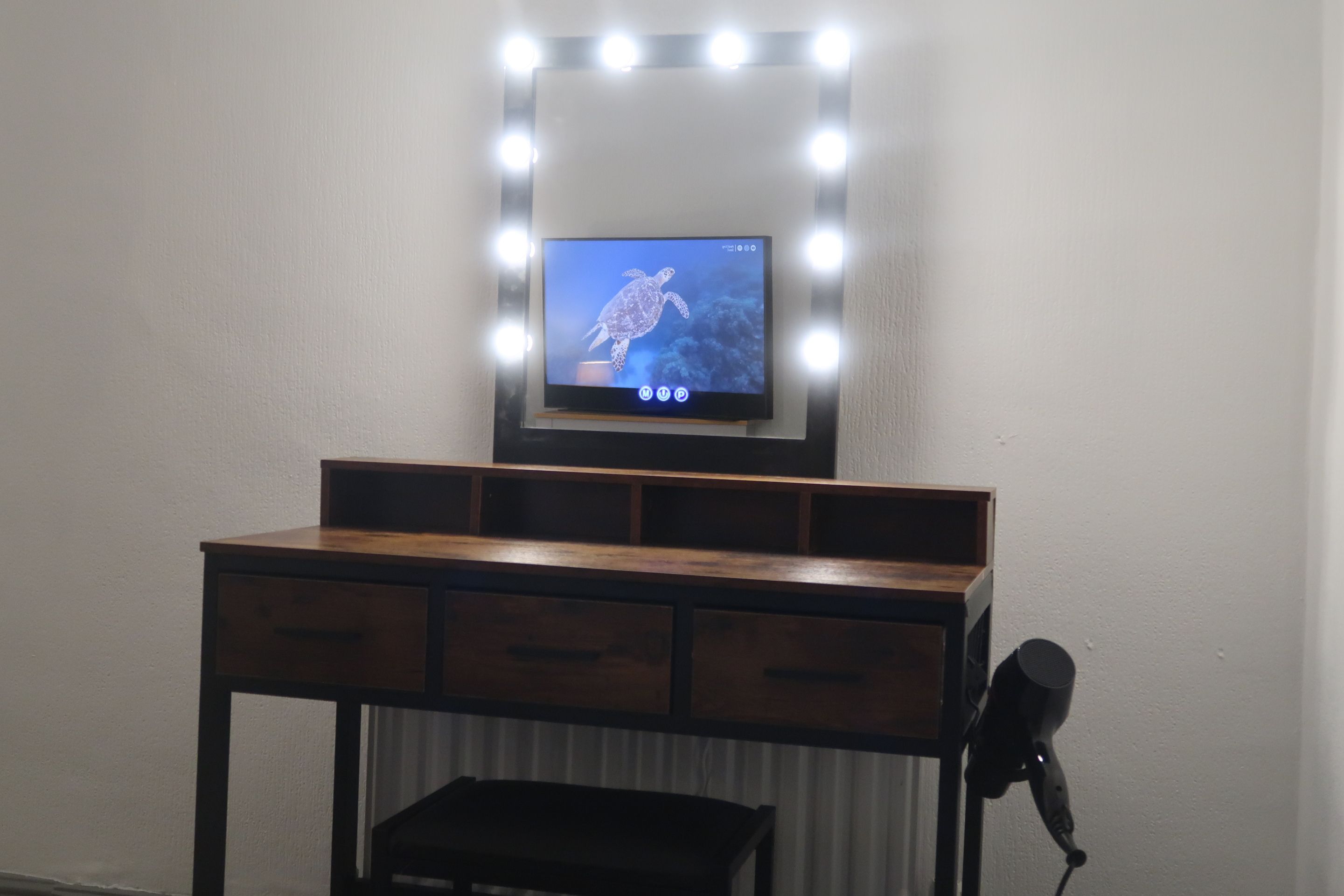 Un tocador con espejo e iluminación, un televisor encima y un micrófono sobre un soporte.