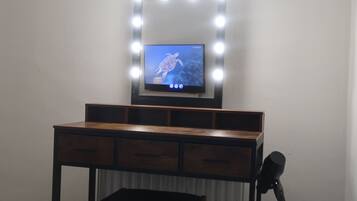 Un tocador con espejo e iluminación, un televisor encima y un micrófono sobre un soporte.