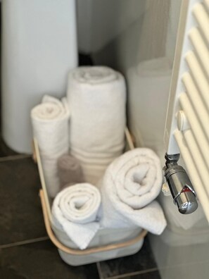 A bathroom with a towel rack holding rolled towels and a glass shower enclosure. - Abbey House Bed and Breakfast (Penrith)