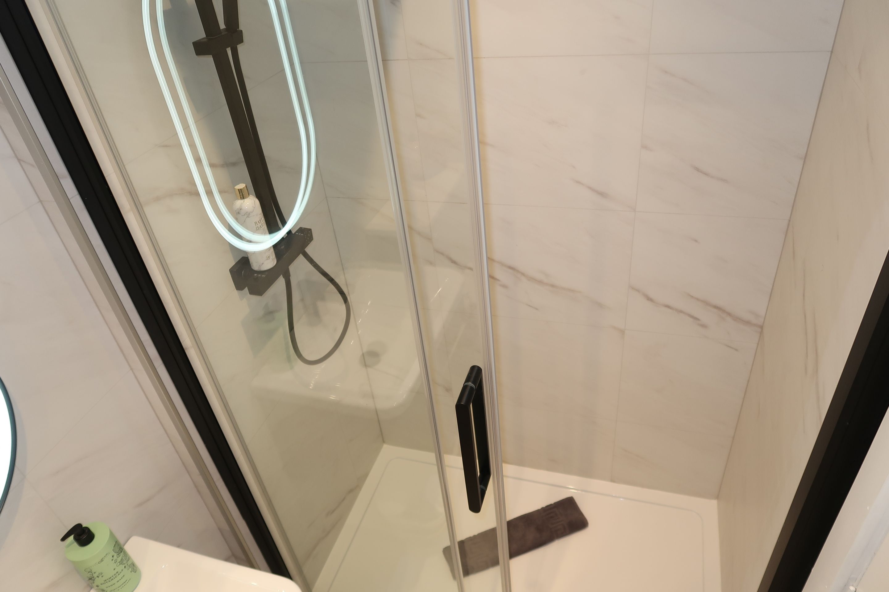 A glass-enclosed shower with a handheld showerhead and a handheld bar.