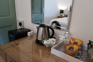 A hotel room with a wooden table, a kettle, a glass of milk, a packet of cheese biscuits, and a mirror reflecting the room. - Abbey House Bed and Breakfast (Penrith)