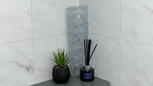 A bathroom with white marble tiles, a grey cabinet, a potted plant, and a reed diffuser. - Abbey House Bed and Breakfast (Penrith)