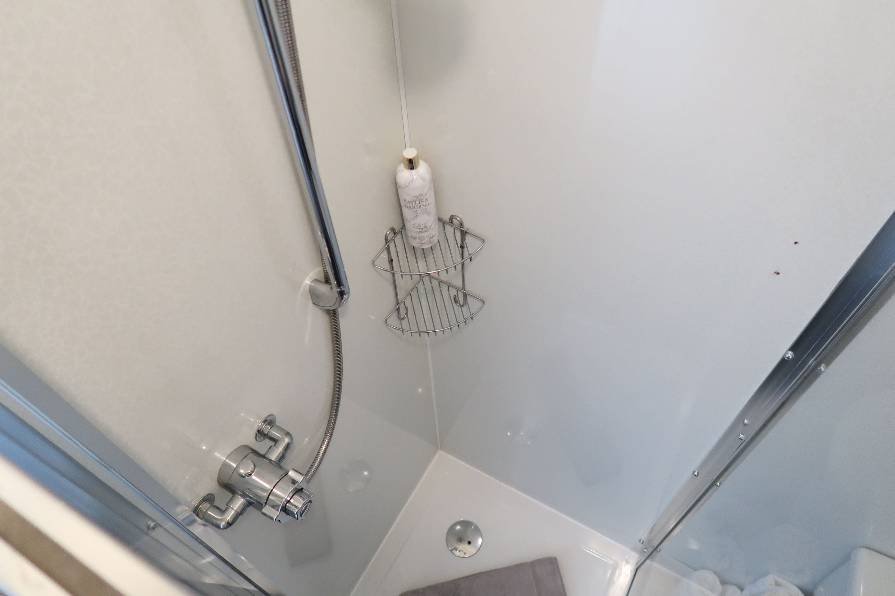 A shower with a handheld showerhead, a handheld soap dispenser, and a metal shower tray.