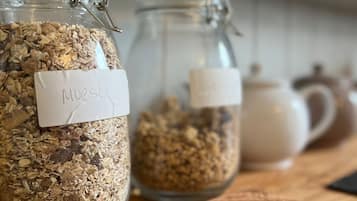 Three glass jars with labels on a wooden surface, a white mug, and a shelf with various items in the background.