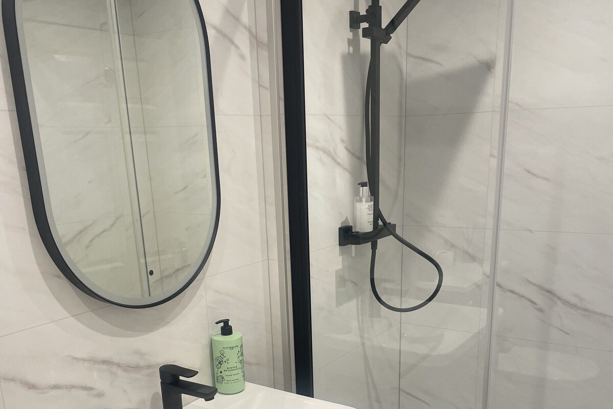 A bathroom with a white sink, a mirror, a shower, and a towel rack.