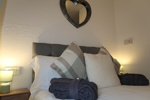 Una cama bien hecha con un espejo con forma de corazón encima, una almohada y una toalla enrollada al lado.