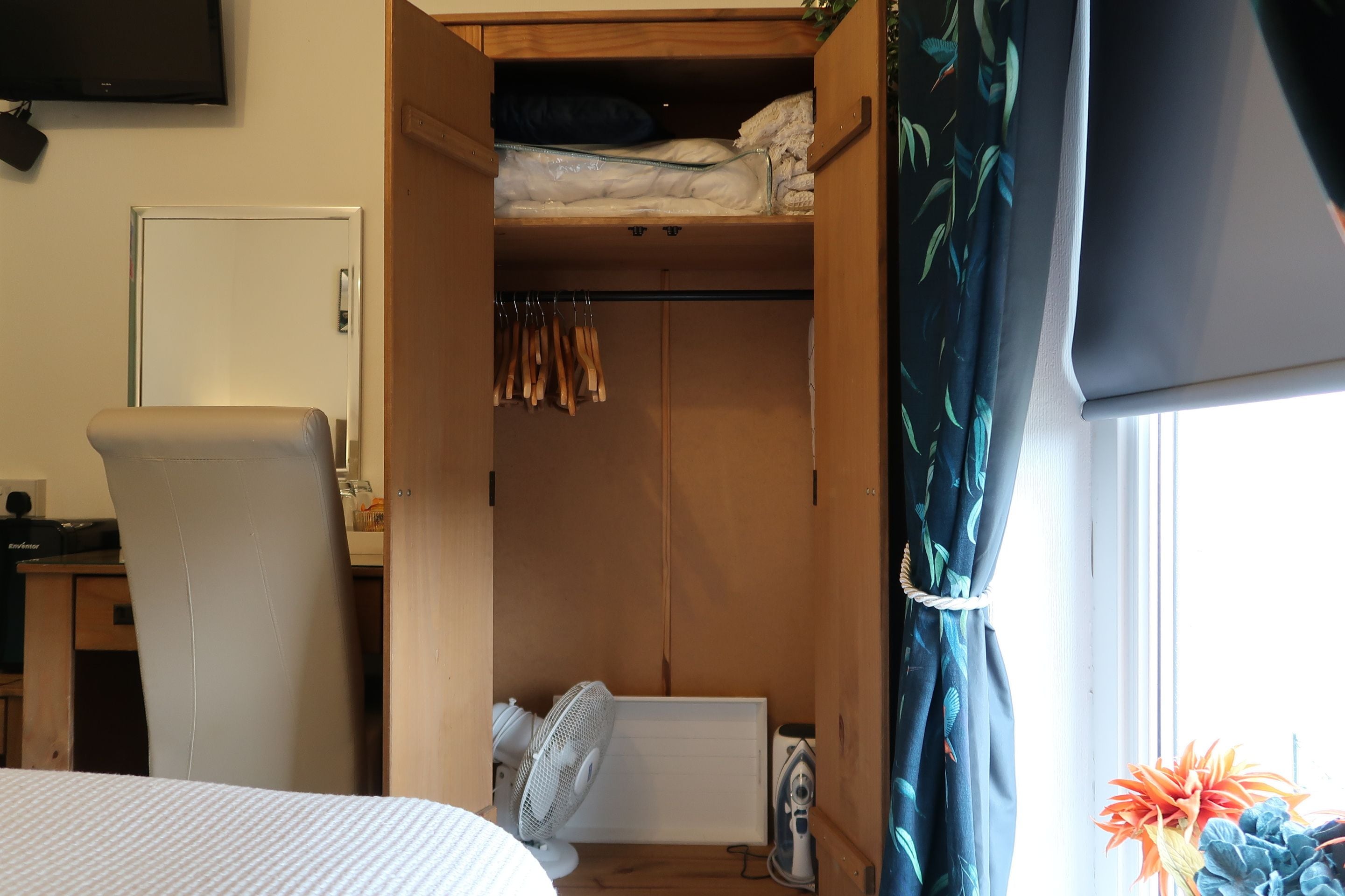 Un dormitorio con cama, armario de madera, radiador y ventilador.