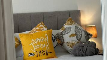 Een bed met een wit hoofdeinde, twee decoratieve kussens en een bedlamp.