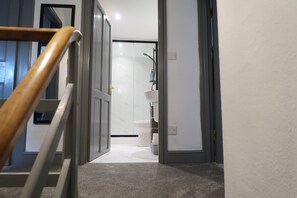 A hallway with a wooden handrail, a white door, and a bathroom with a white sink and towel rack. - Abbey House Bed and Breakfast (Penrith)