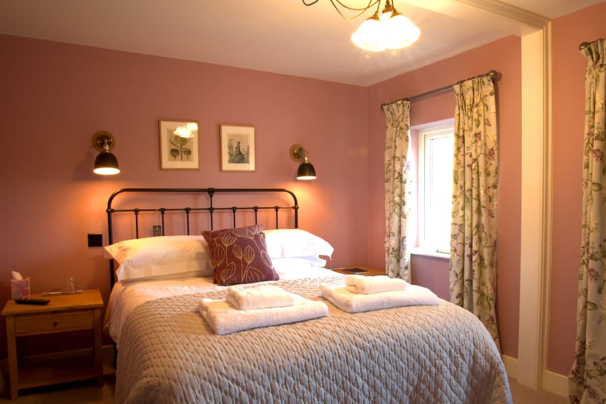 A bedroom with a bed, a nightstand, a lamp, and a window with curtains.