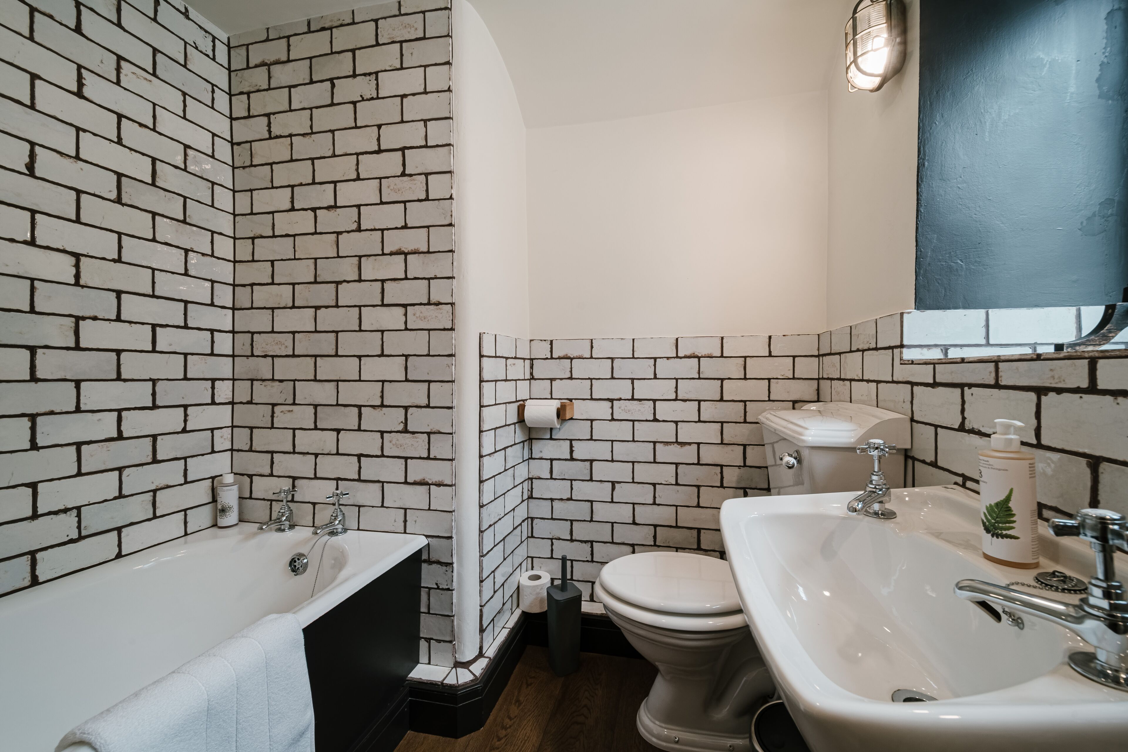 Ein Badezimmer mit weißer Ziegelwand, einer Badewanne, einer Toilette und einem Waschbecken.