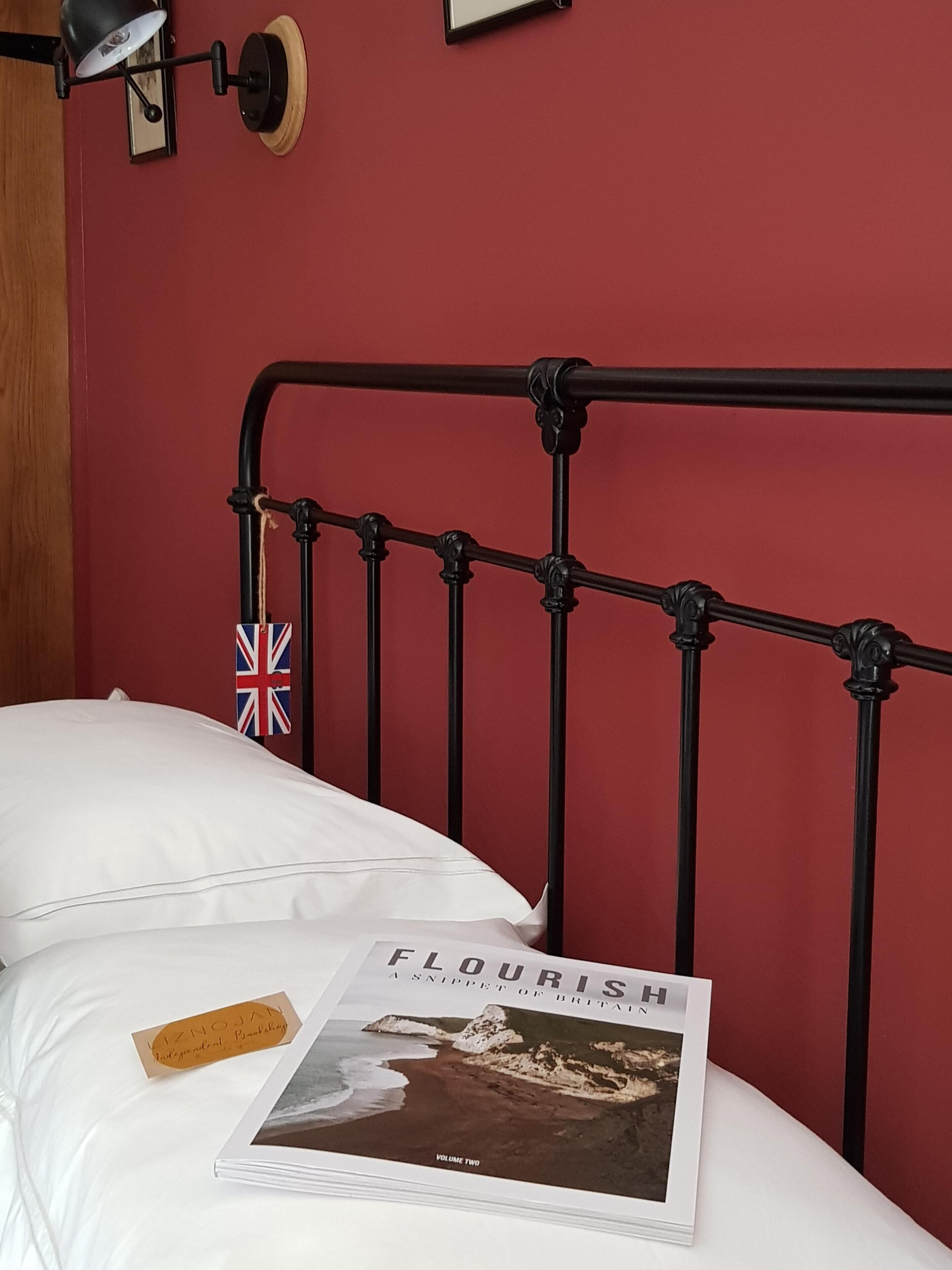 Una cama con estructura metálica negra, ropa de cama blanca y un libro titulado 'Flourish' sobre la cama.