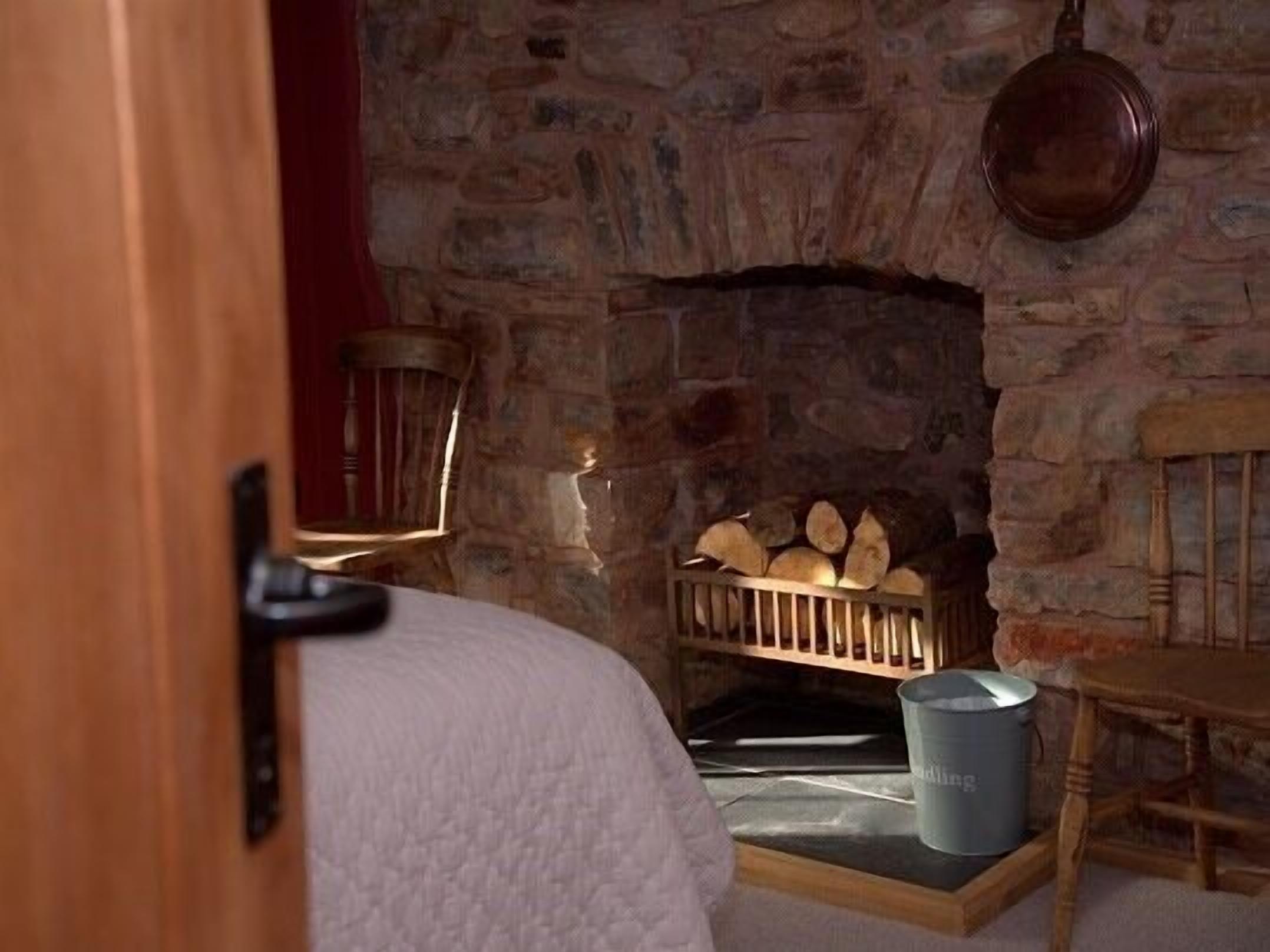A stone fireplace with logs, a metal bucket, and a wooden chair.