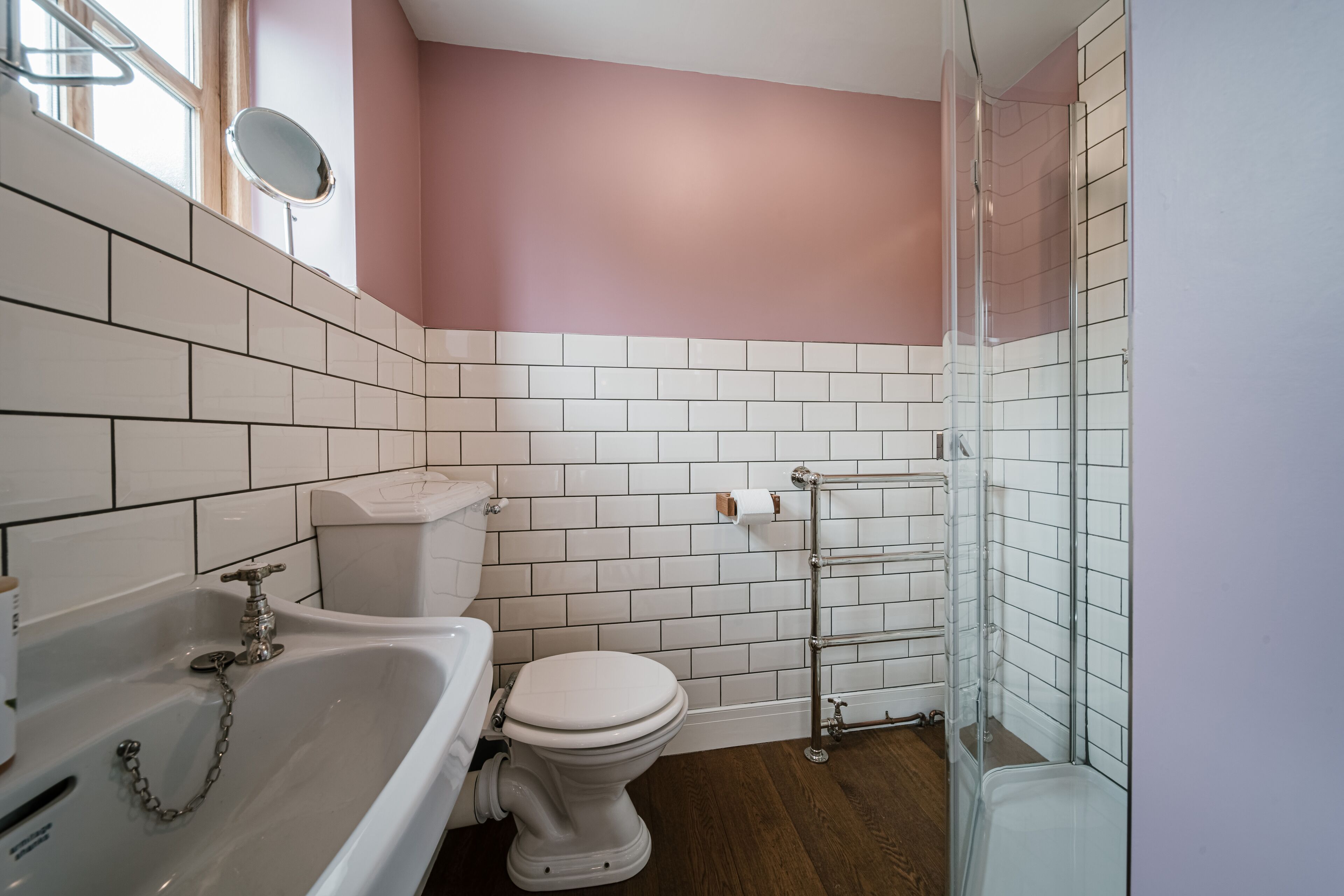 Un baño con azulejos blancos, una pared rosa, una bañera, un inodoro y una cabina de ducha de cristal.