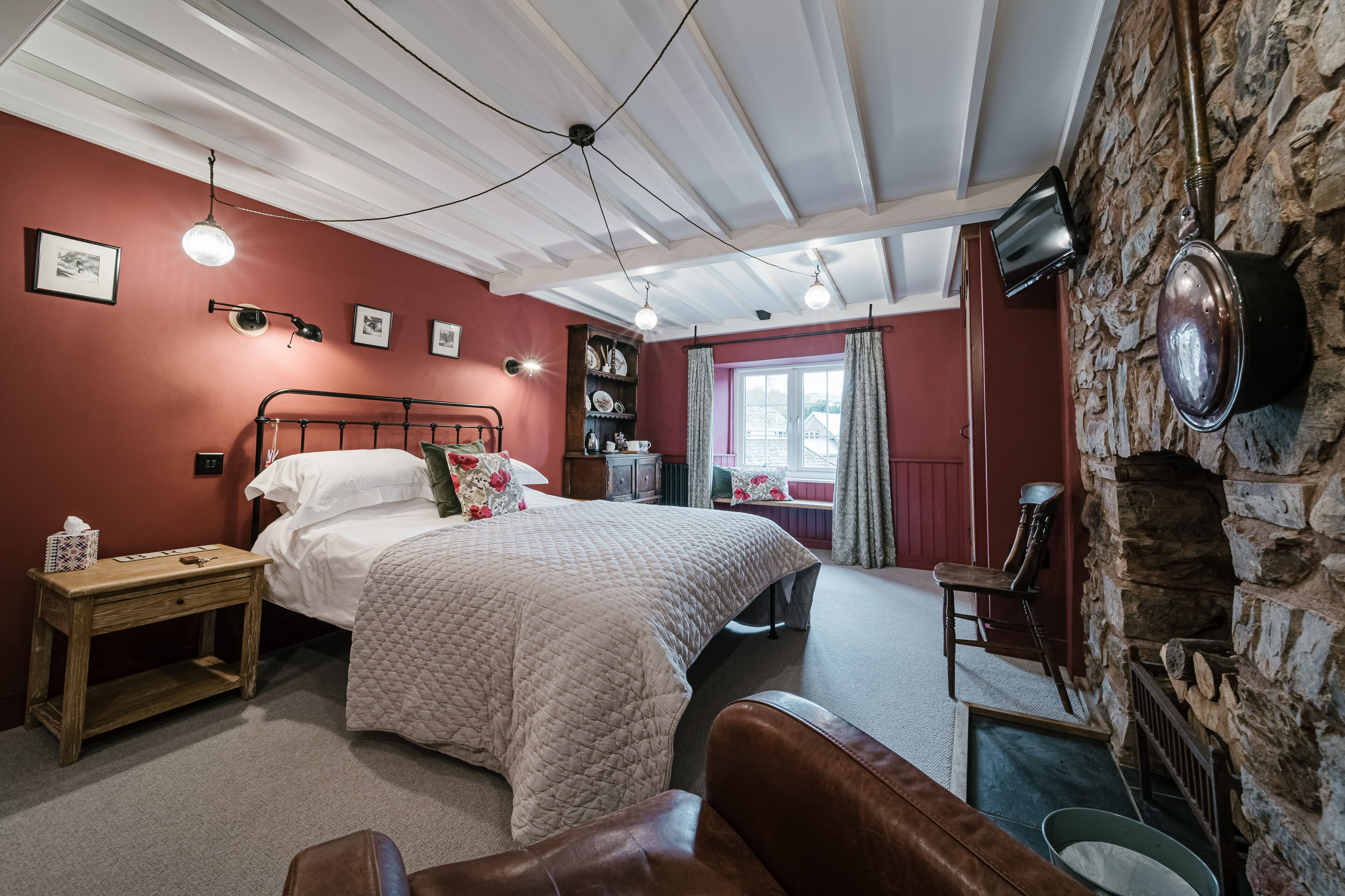 A cozy bedroom with a bed, a wooden nightstand, a stone wall, and a stone fireplace.