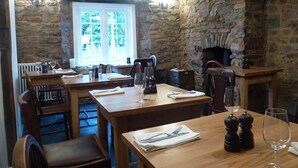 A restaurant with stone walls, wooden tables, and a fireplace. - Bridge House (Tiverton)