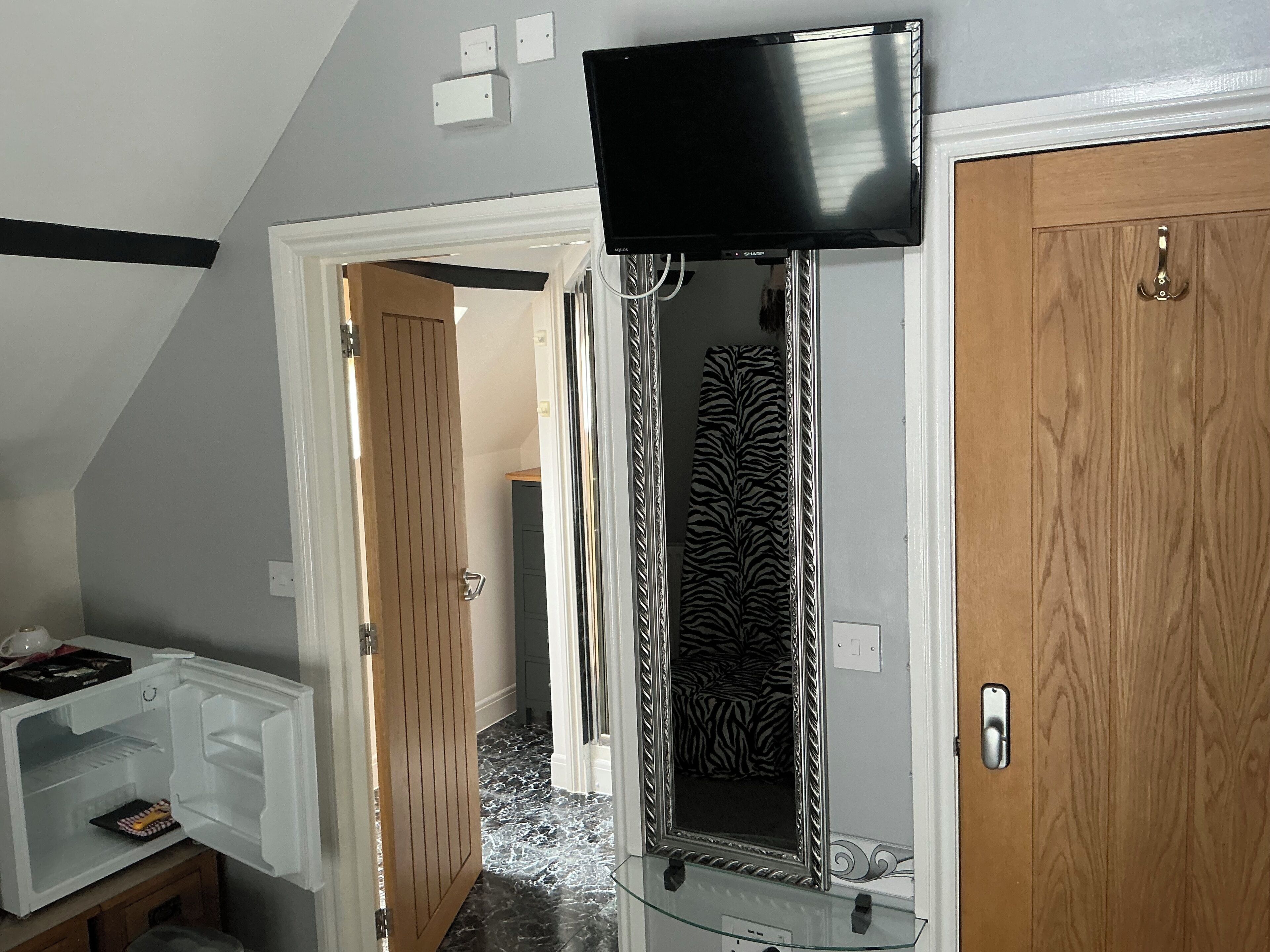 Un couloir avec une porte donnant sur une salle de bain, un miroir et un téléviseur fixé au mur.
