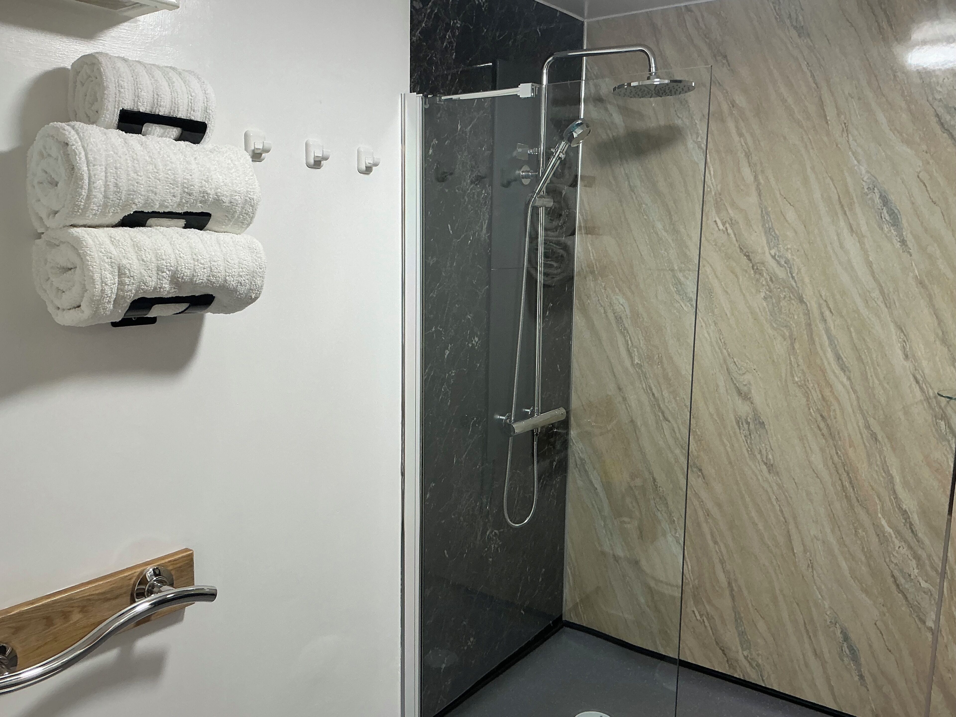 A modern bathroom with a glass-enclosed shower, marble walls, and neatly rolled towels on a rack.