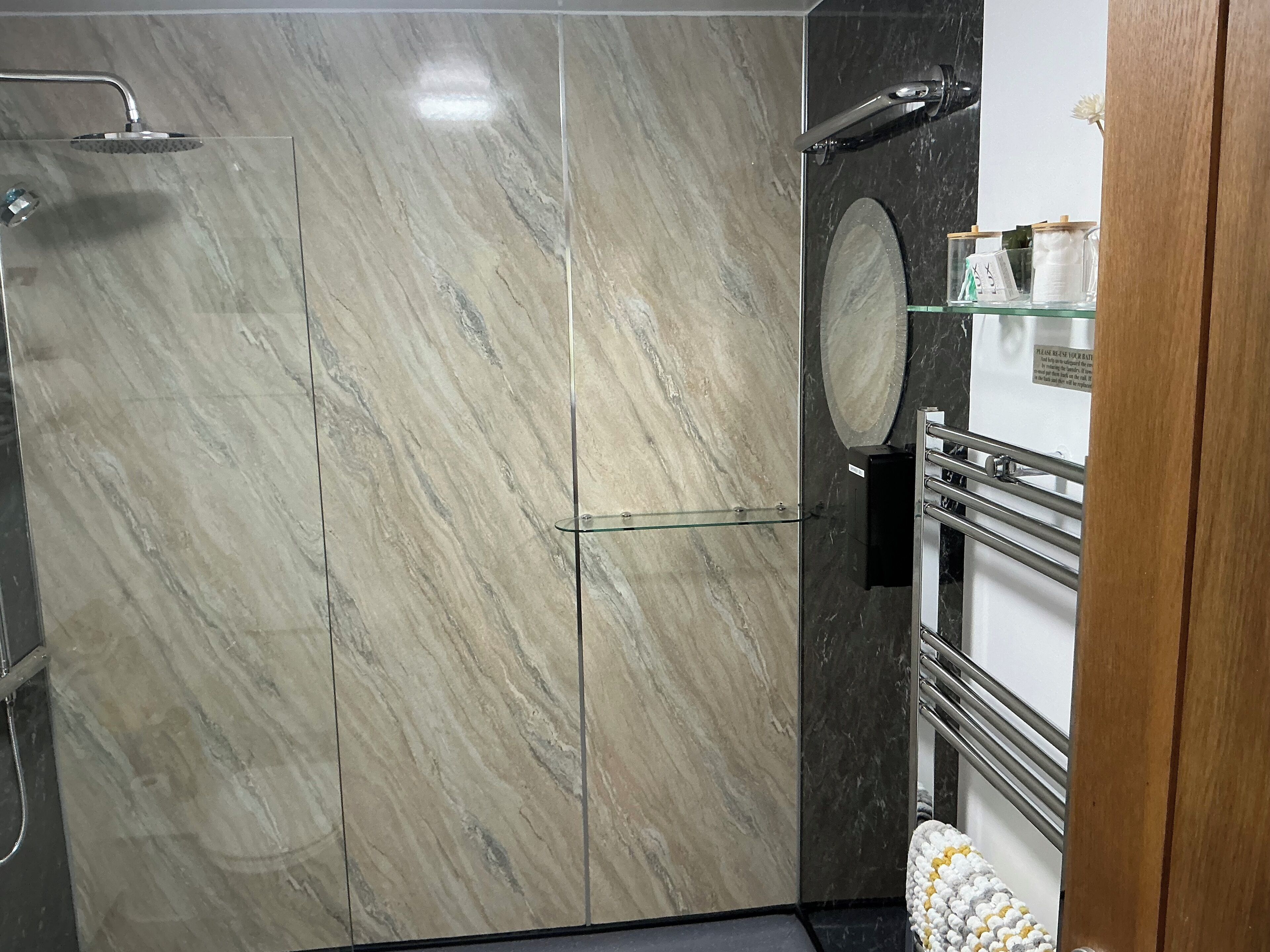 A bathroom with a shower, a glass shelf with toiletries, and a mirror.