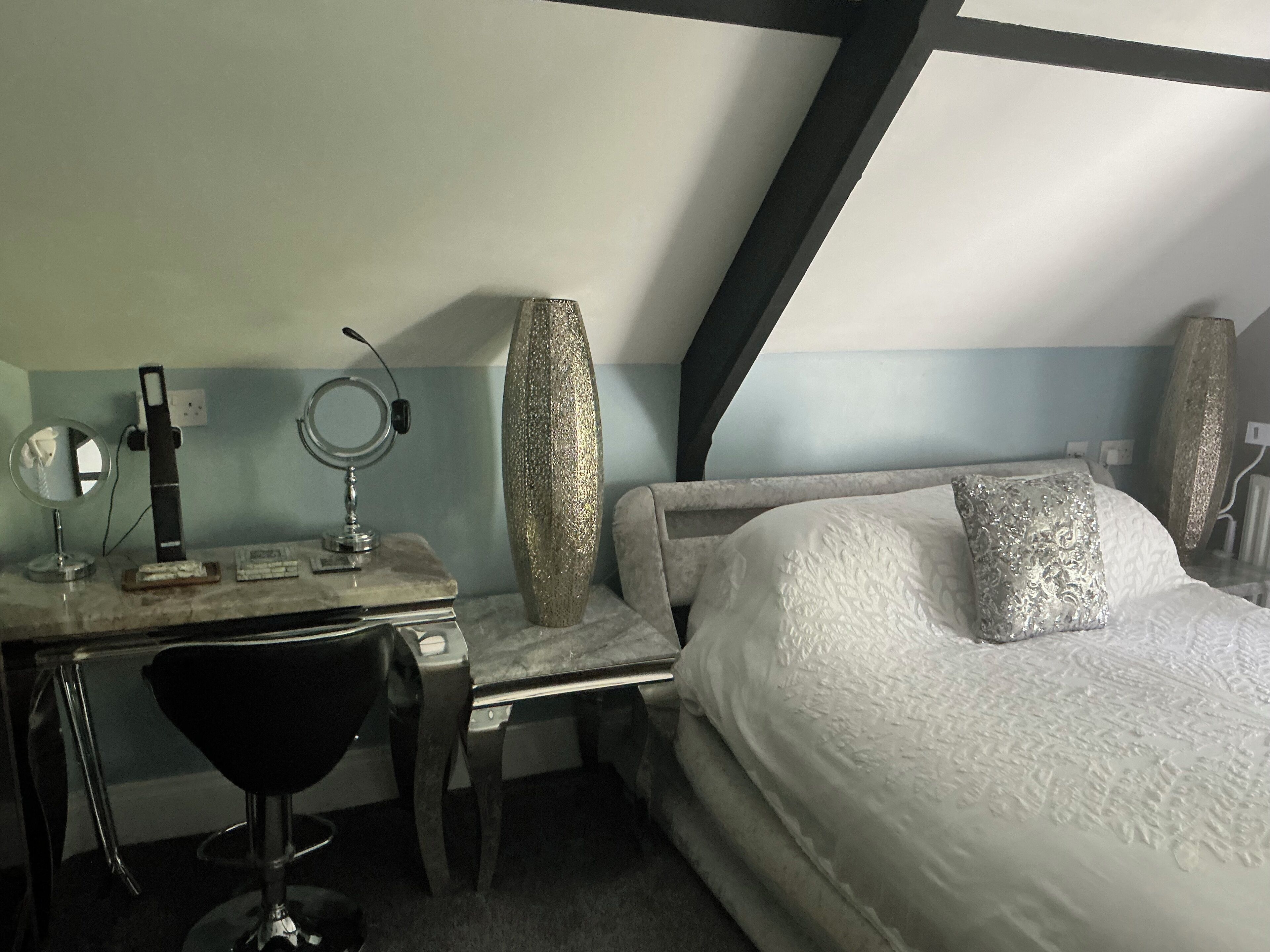 Une chambre à coucher comprenant un lit, un bureau avec une chaise, un miroir et un vase décoratif.