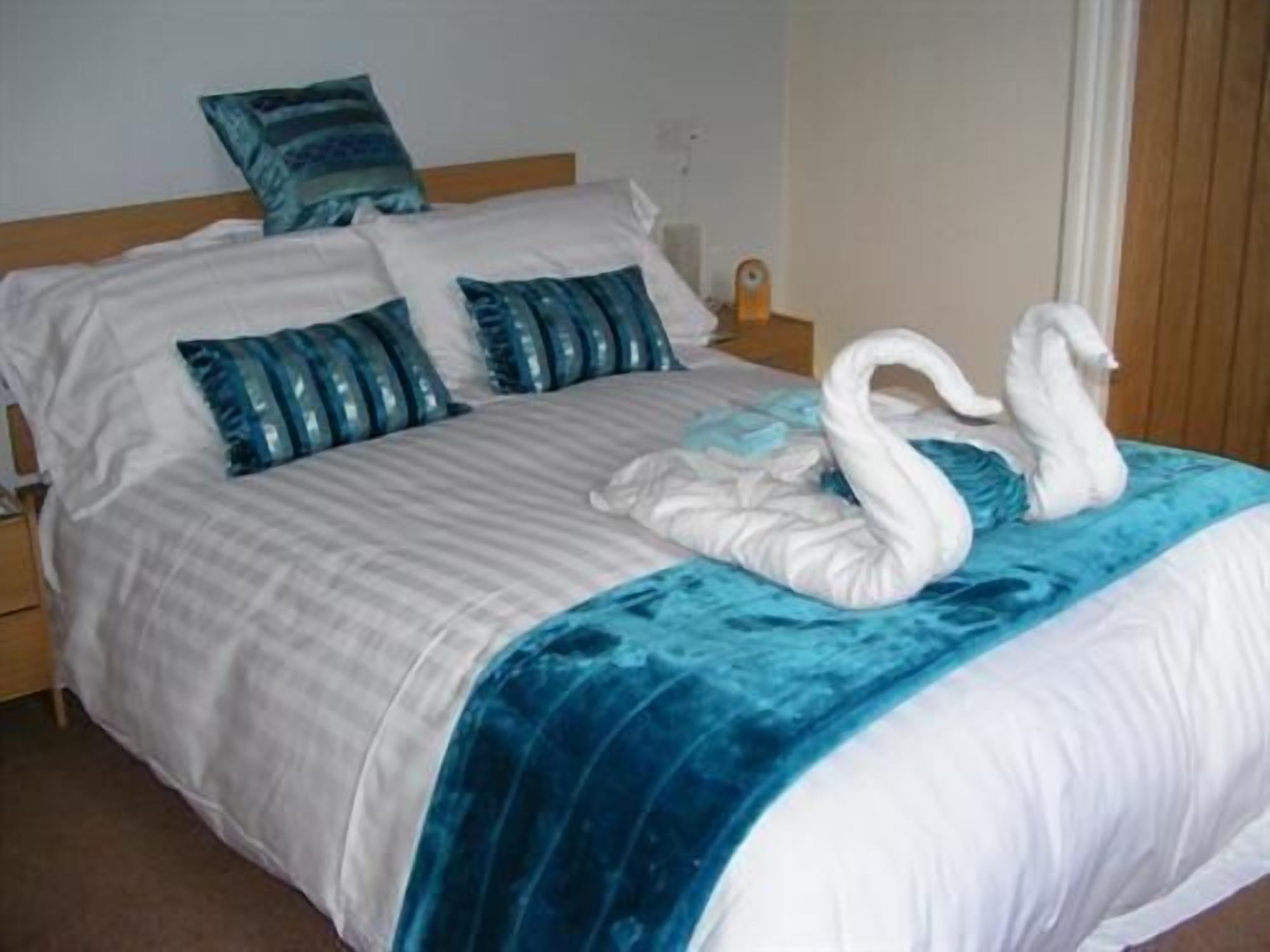 A neatly made bed with a blue blanket and two swan-shaped pillows.