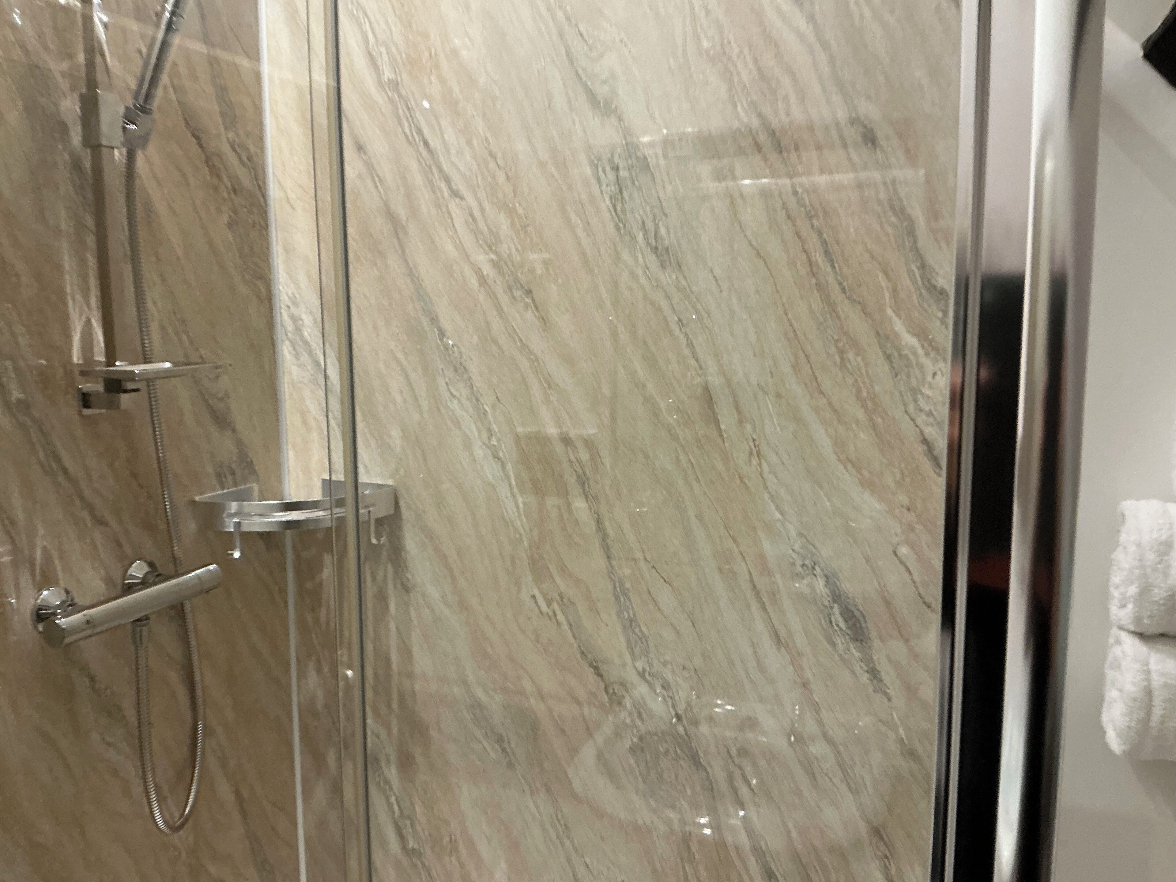 A glass-enclosed shower with a marble wall, a handheld showerhead, and a wall-mounted faucet.