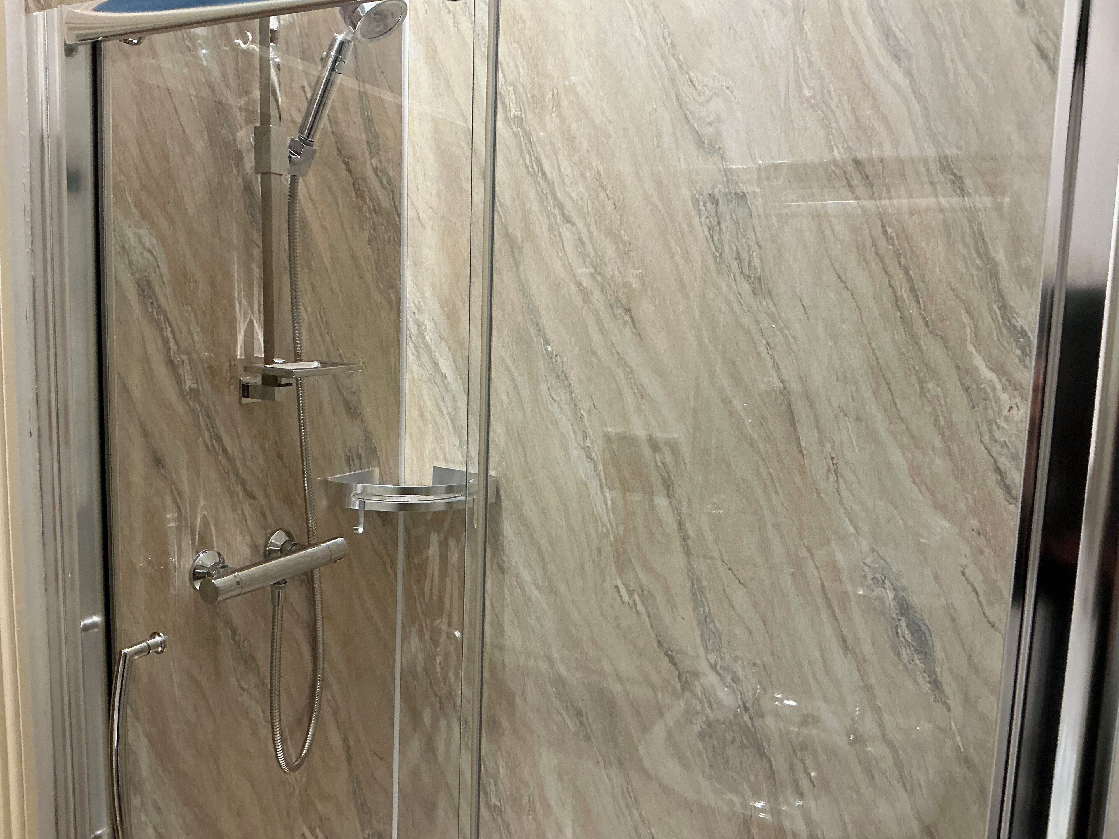 A glass-enclosed shower with a marble wall, a handheld showerhead, and a handheld shower hose.