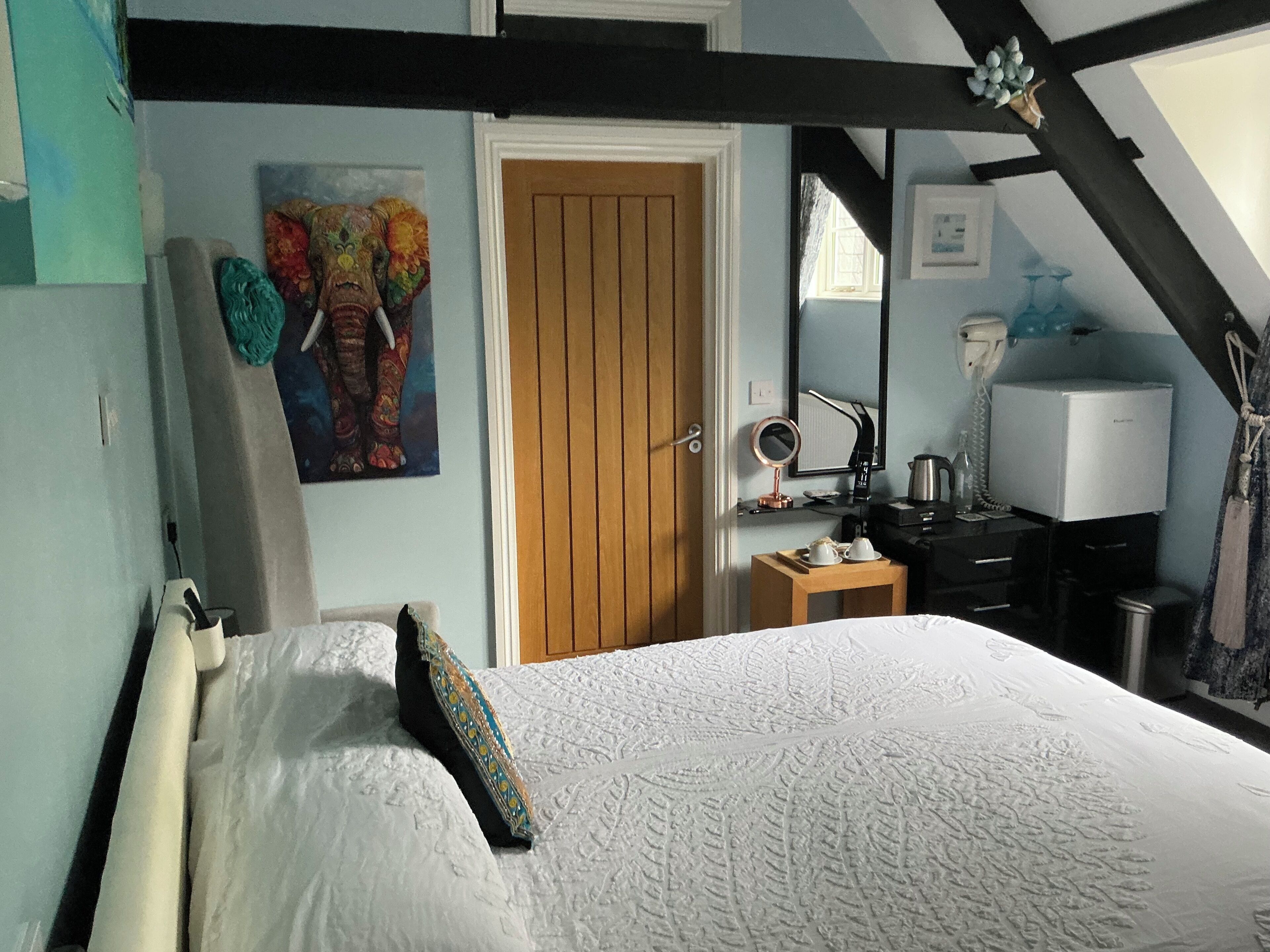 Een slaapkamer met een bed, een houten deur, een bureau met spiegel, een waterkoker en een televisie.