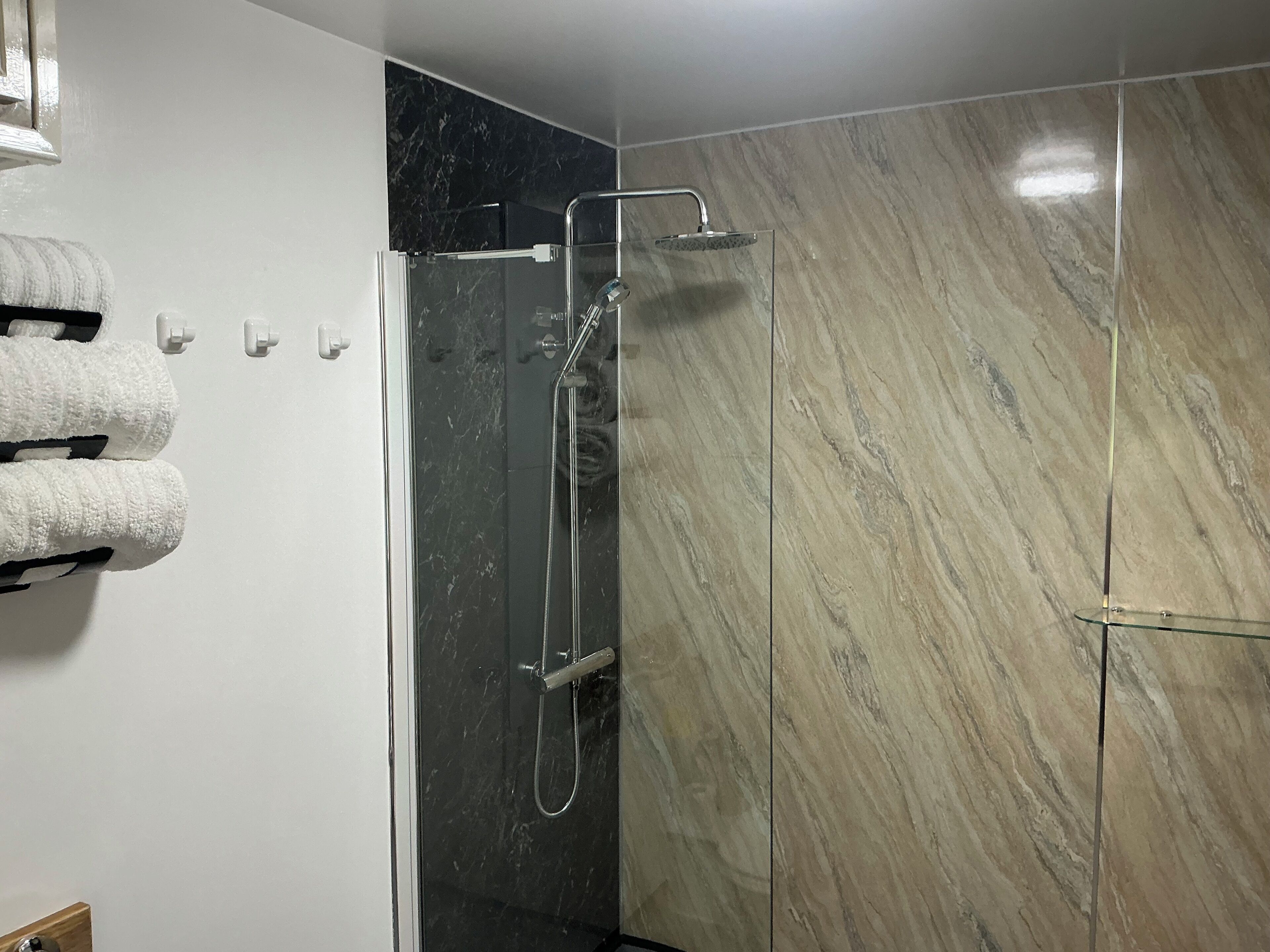A modern bathroom with a glass-enclosed shower, marble walls, and neatly arranged towels.