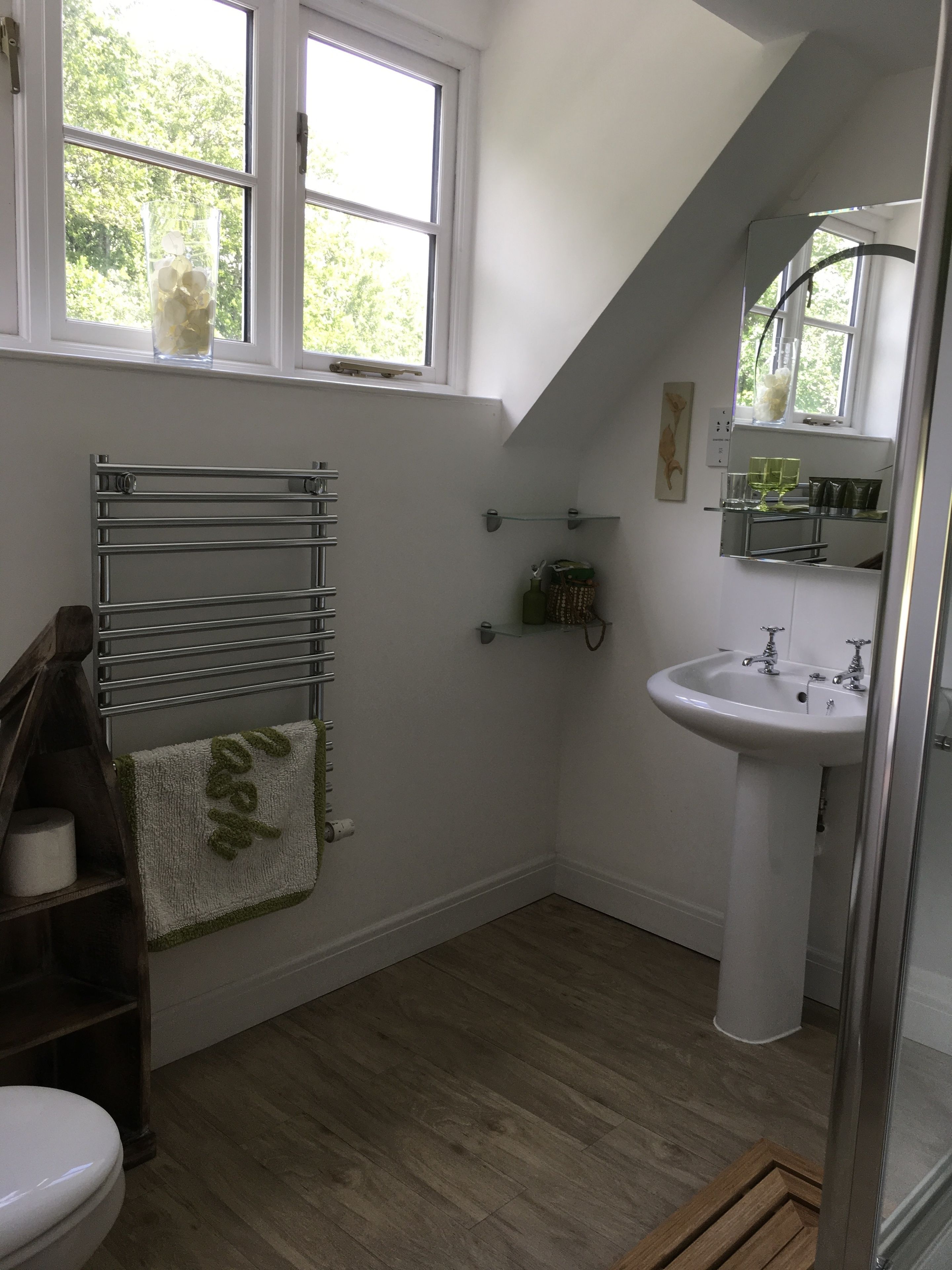 A bathroom with a wooden floor, a white sink, a towel rack, and a window with a view of trees.