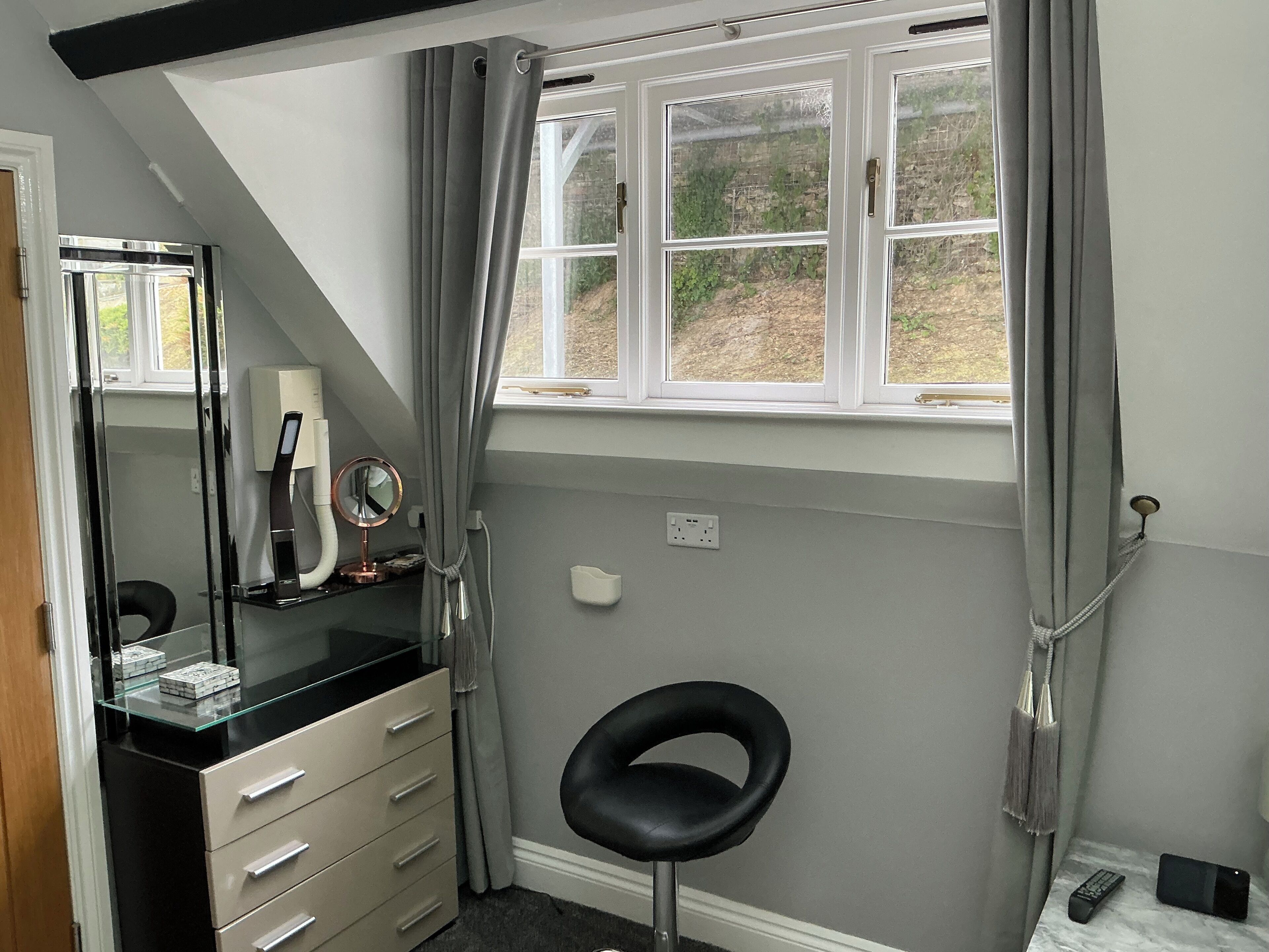 A bathroom with a vanity, a mirror, a black chair, a window with curtains, and a marble countertop.