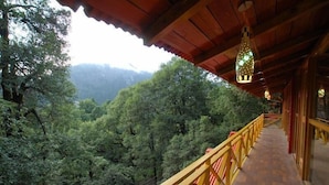 Un balcon en bois avec une rambarde jaune donnant sur une vallée boisée.