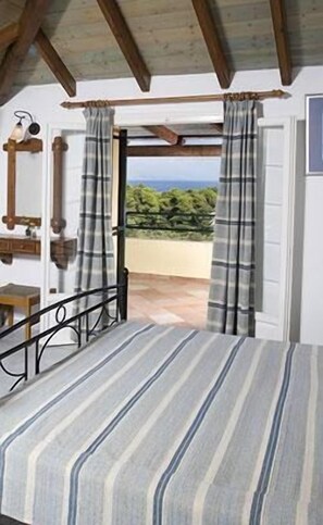 Een slaapkamer met een bed, uitzicht op groen en een balkon.